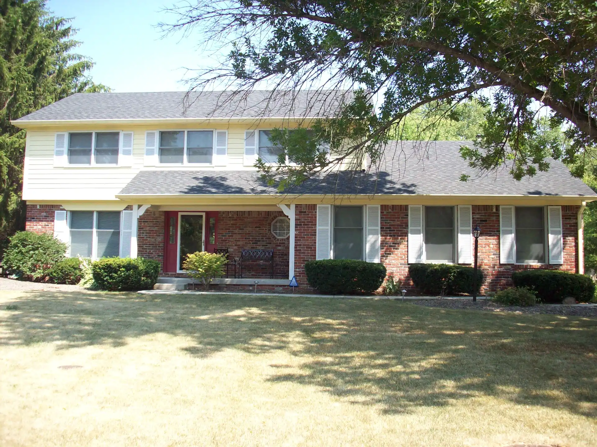 Two-story home repainted in warm cream siding with white shutters and a red front door