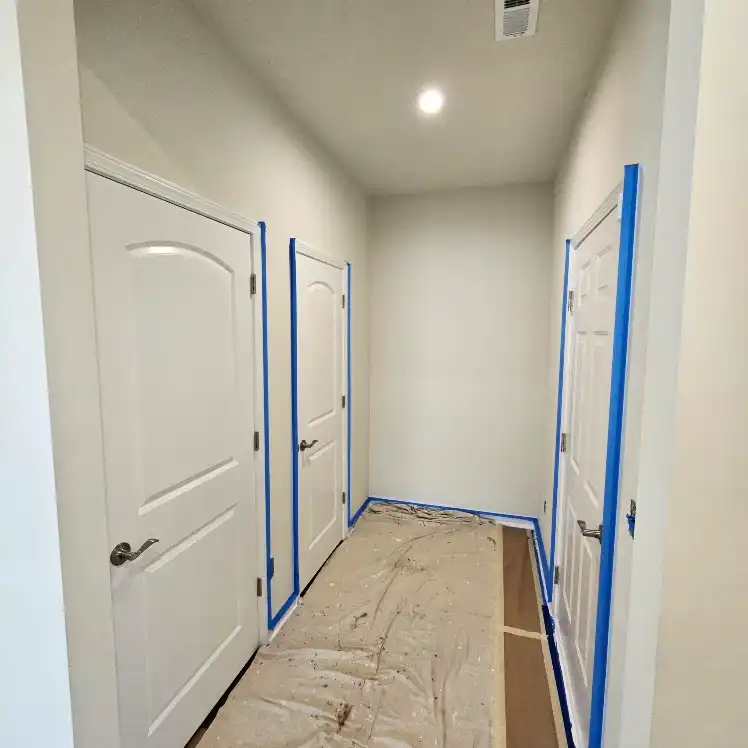 Hallway prepped for painting with blue tape around door frames and drop cloths covering the floor