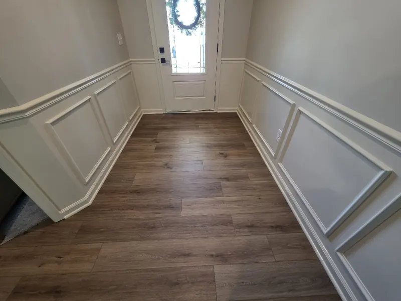 View down the entry hall to the front door, framed by white box moulding panels and chair rail on both sides