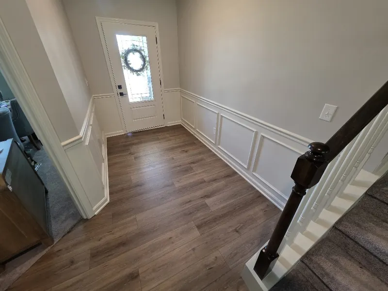 Entry hall with white box moulding and chair rail continuing along the staircase wall toward the front door