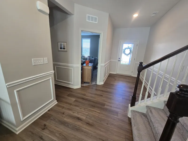 Same foyer view after installation, white box moulding panels under a white chair rail on the gray walls beside the staircase