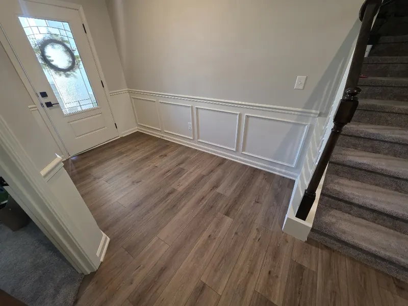 Entry with white box moulding and chair rail running from the front door to the carpeted staircase over wood-look flooring