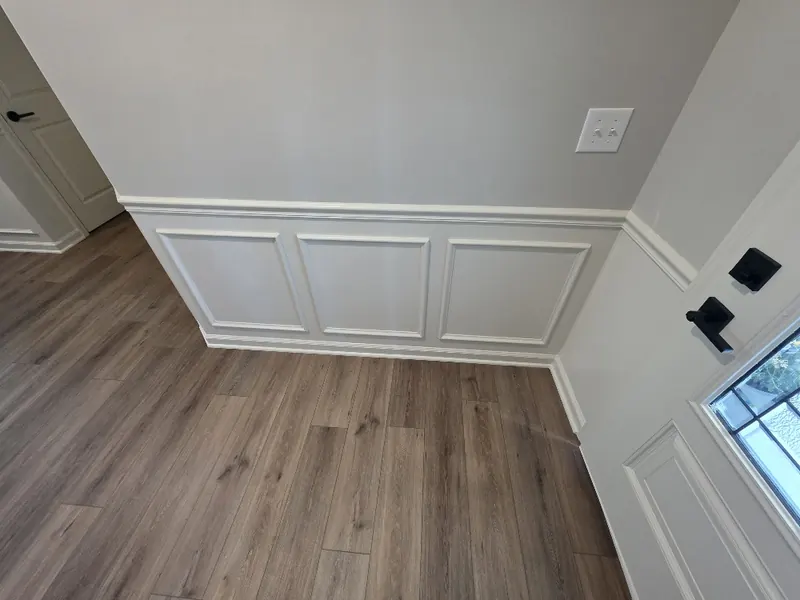Close view of three evenly spaced white box moulding panels under a white chair rail on a light gray wall