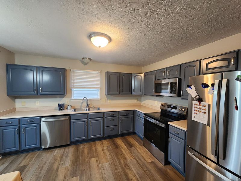 Finished kitchen with slate blue painted upper and lower cabinets, silver pulls, stainless steel appliances and wood-look flooring