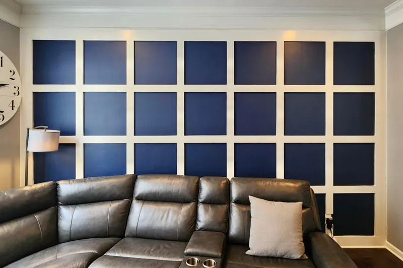 Finished judge's paneling with boxes painted Sherwin-Williams Naval (SW 6244) and grid trim in Pure White (SW 7005) behind a leather sectional