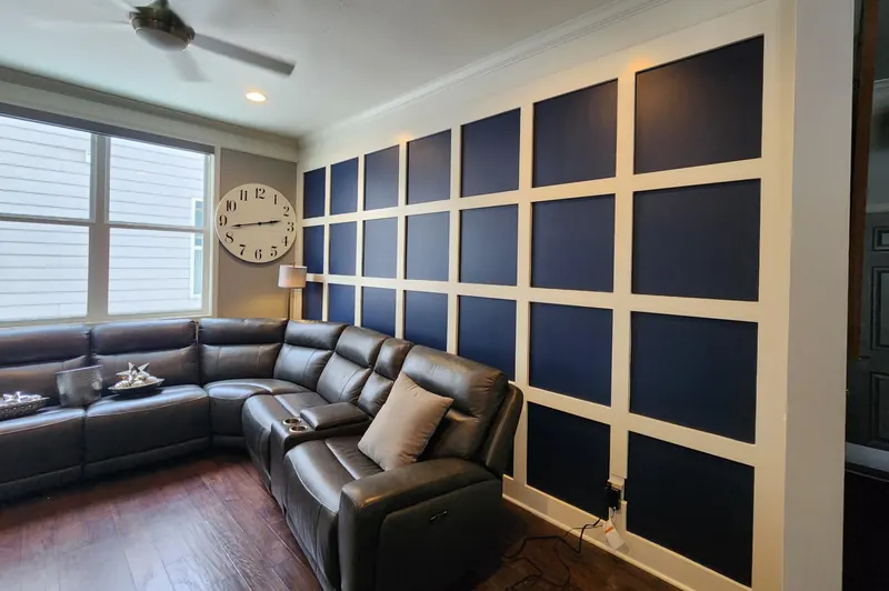 Right-angle view of the family room with a full judge's paneling accent wall in Sherwin-Williams Naval (SW 6244) and Pure White (SW 7005) trim beside a window