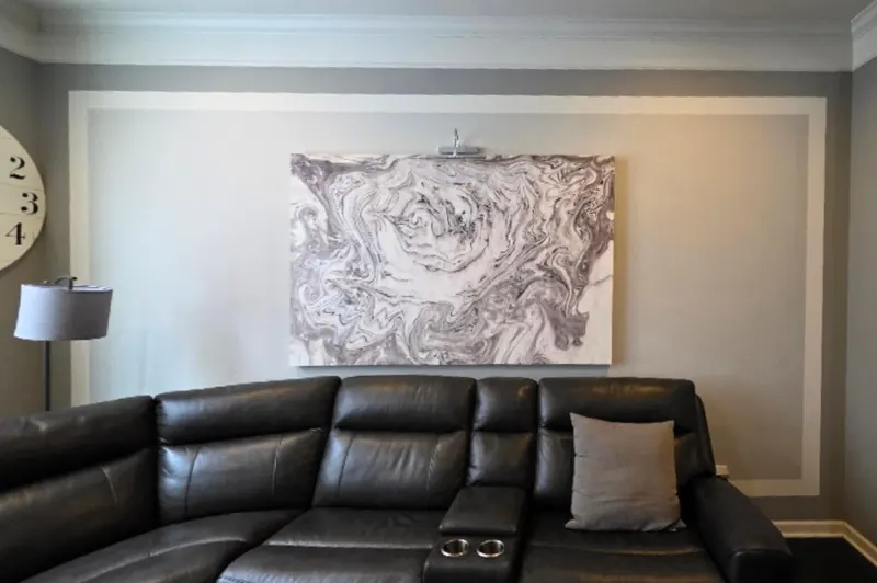 Family room wall before judge's paneling, painted gray with one large white moulding frame, abstract canvas art and a dark leather sectional