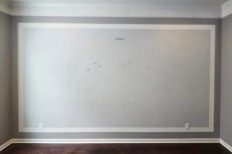 Empty gray family room wall inside the original white moulding frame, cleared of art and furniture before the judge's paneling layout