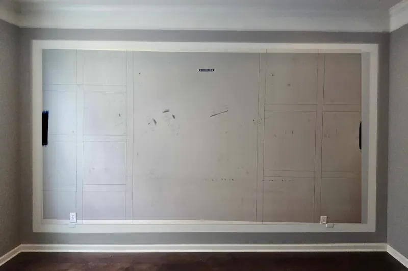 Cleared gray wall with the judge's paneling grid layout sketched in pencil inside the existing moulding frame