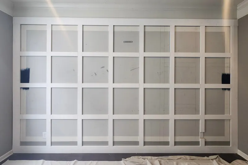 Full-height judge's paneling grid of square boxes installed and caulked on a family room wall, ready for paint