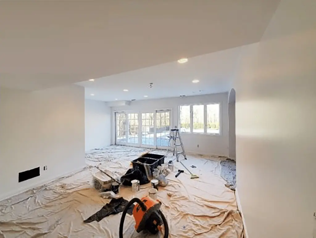Finished basement mid-project, with walls painted white and the floor covered in drop cloths