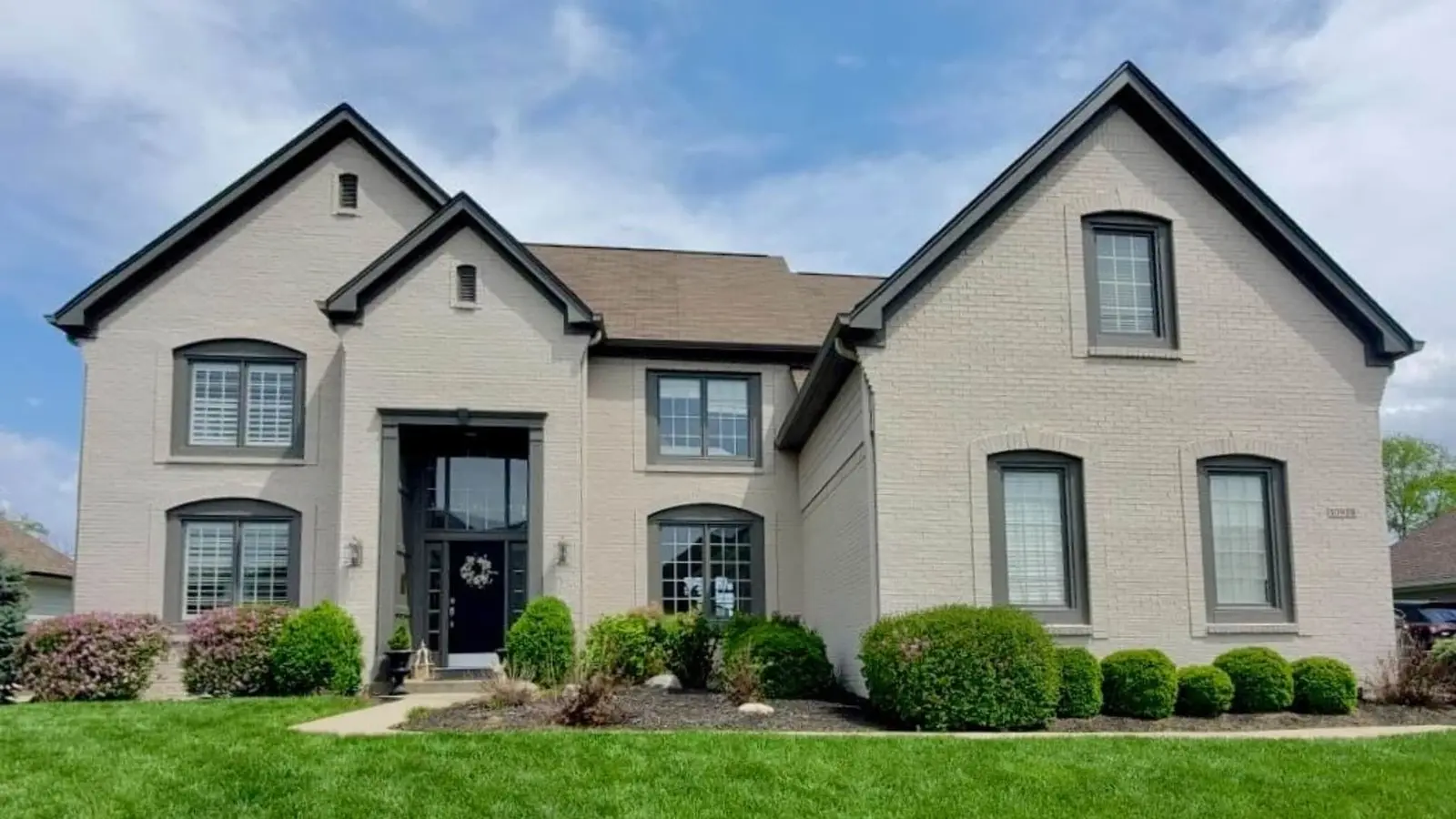 Two-story home with light gray painted brick and dark gray windows, trim and gutters