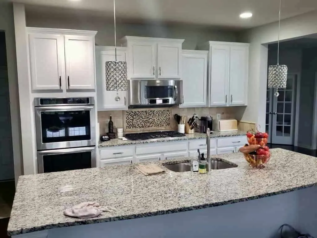 Kitchen with shaker cabinets painted white, a granite-topped island and a mosaic tile backsplash