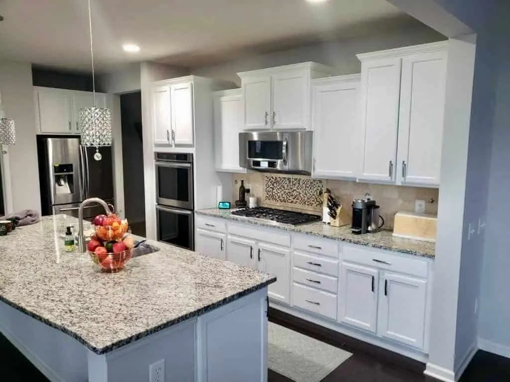 Kitchen with shaker cabinets painted white, a granite-topped island and a mosaic tile backsplash