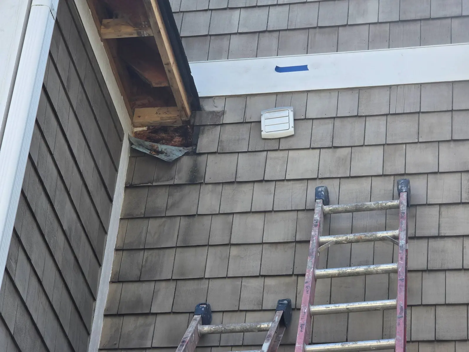 Water-damaged cedar shingle siding near the roofline and trim