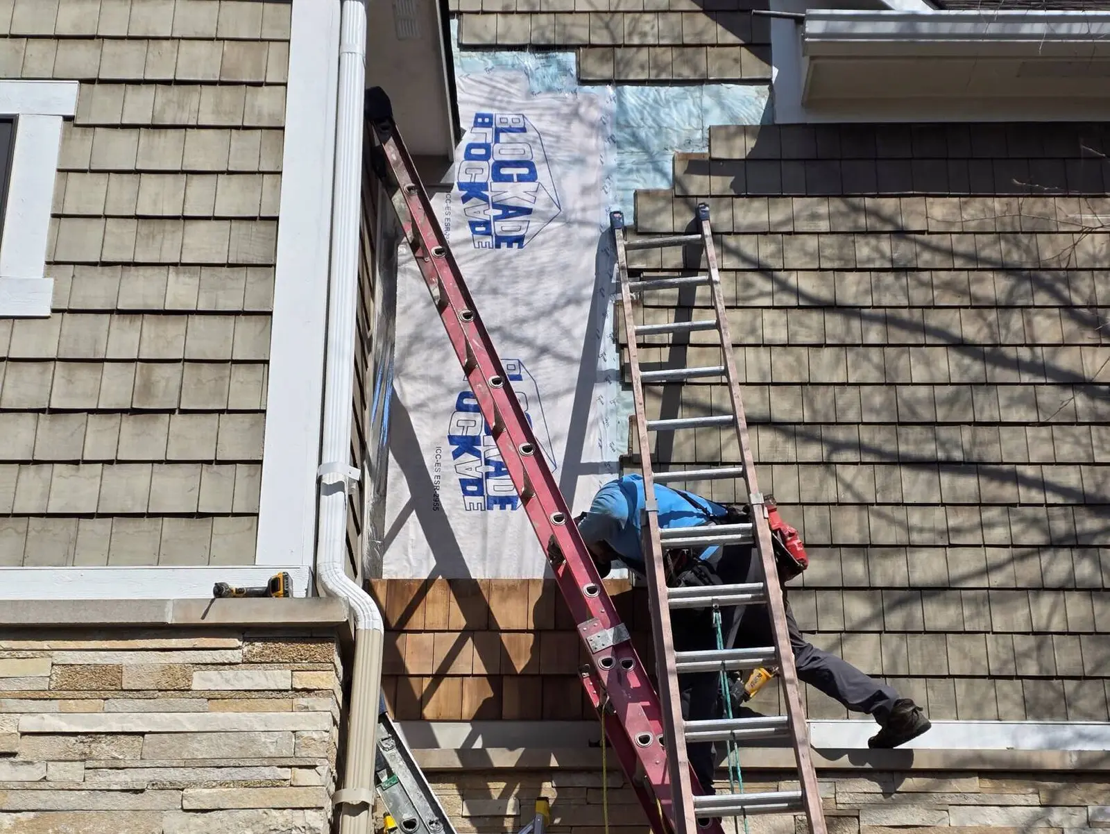 Carpenter on a red ladder installing house wrap and new cedar shingles