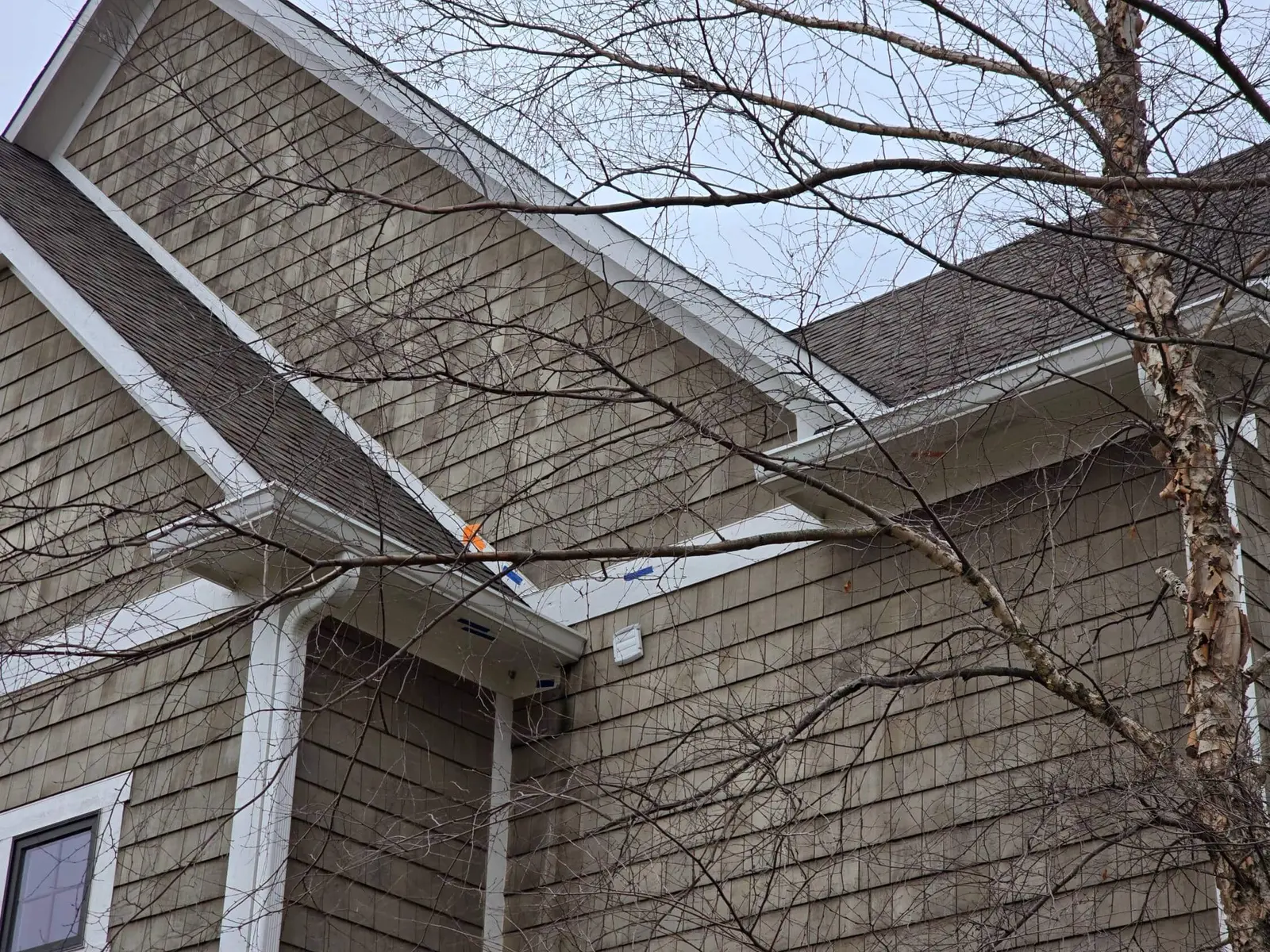 Cedar shingle siding next to a white gutter, with blue and orange tape marking areas to repair