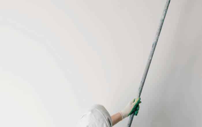 Technician using an extension pole and roller to apply white paint to a high residential ceiling.