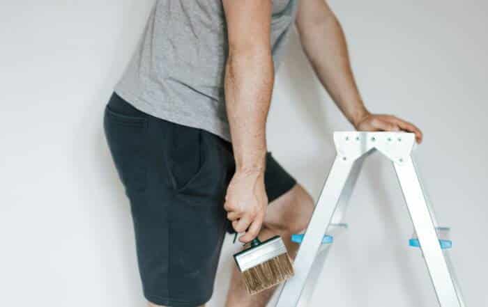 Painter on a step ladder cutting in a sharp line along the ceiling and trim.