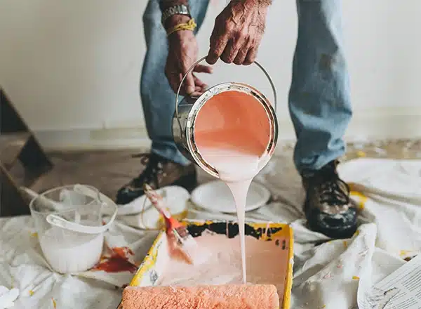 close-up of a house painter pouring peach-colored interior paint into a tray, showing professional preparation for a home renovation project in carmel, indiana.